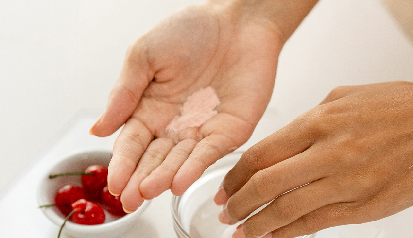 A woman shakes Eminence Organics Barbados Enzyme Cleansing Powder into the palm of her cupped hand. 