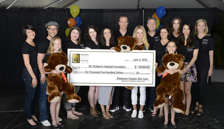 A crowd of people, including children holding teddy bears, pose with a giant cheque made out to BC Children's Hospital Foundation. 
