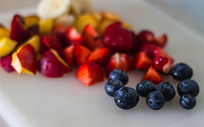 Chopped plums, quartered strawberries and whole blueberries are displayed on a white cutting board