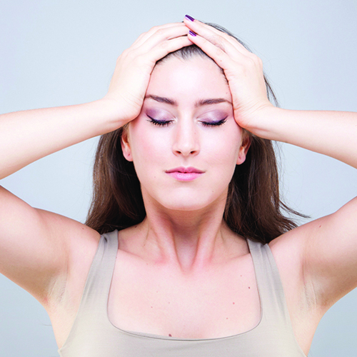 A woman massaging her forehead using the palms of her hands to press into the sides of her face