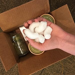 The hand of a woman holds white, dissolvable packing peanuts over a box filled with products ready for shipping.