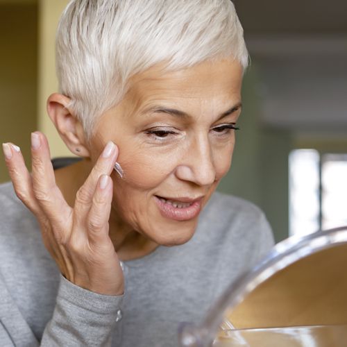 a mature woman applying skin care product to treat acne