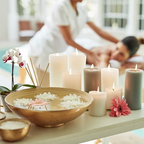 lit candles glow in the foreground while a woman receives a massage at a spa in the background