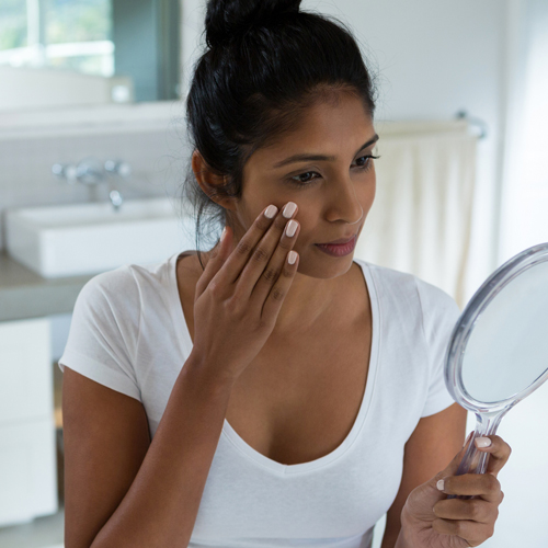 a Latino woman examining her skin