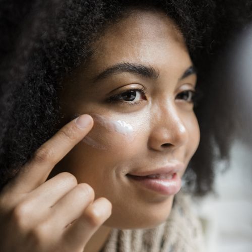 A woman applies eye cream under her right eye