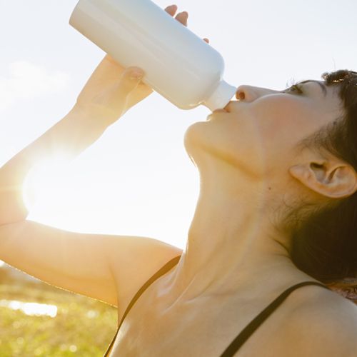 A woman sips water from a bottle while standing outside on a sunny day