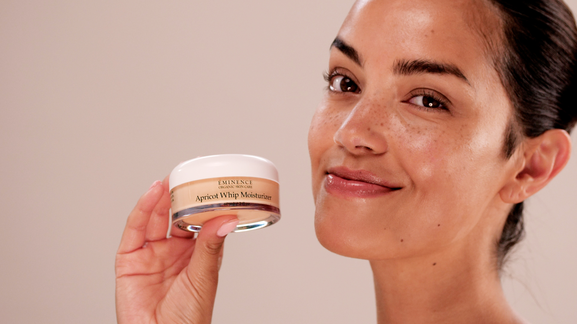 A woman holdnig Eminence Organics Apricot Whip Moisturizer near her face